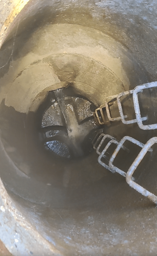 Betonbrønd med stigetrin, hvor vand løber ned i banketten.